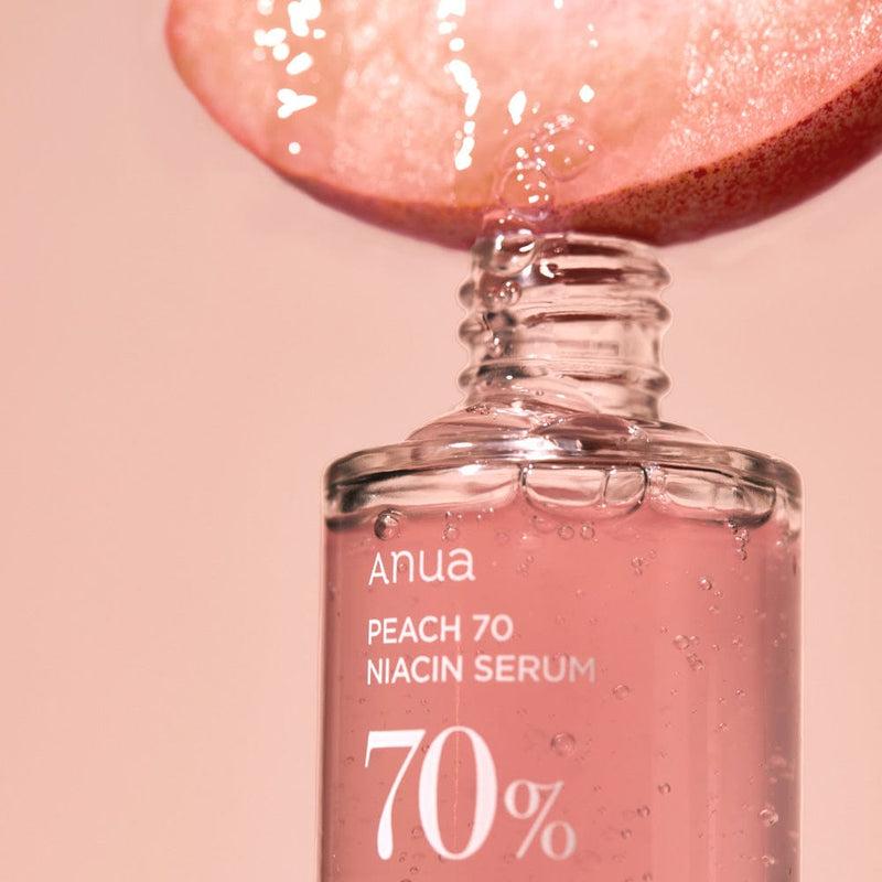 A peach slice drips juice into a clear bottle of ANUA - Peach 70% Niacinamide Serum 30ml. The serum is pink, and the label highlights "70%" in large white text. The background is a soft peach color, creating a cohesive and aesthetically pleasing image perfect for achieving glass skin.