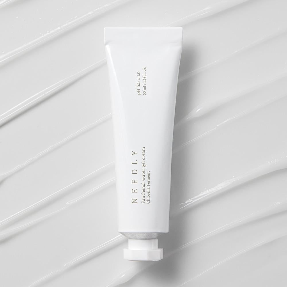 A white tube of NEEDLY - Panthenol Water Gel Cream 50ml with a minimalist label is placed on a textured white background. The partially unscrewed tube reveals the opening, perfect for an oily skin moisturizer. Streaks of the gel cream are smeared on the background, highlighting its skin barrier protection benefits.