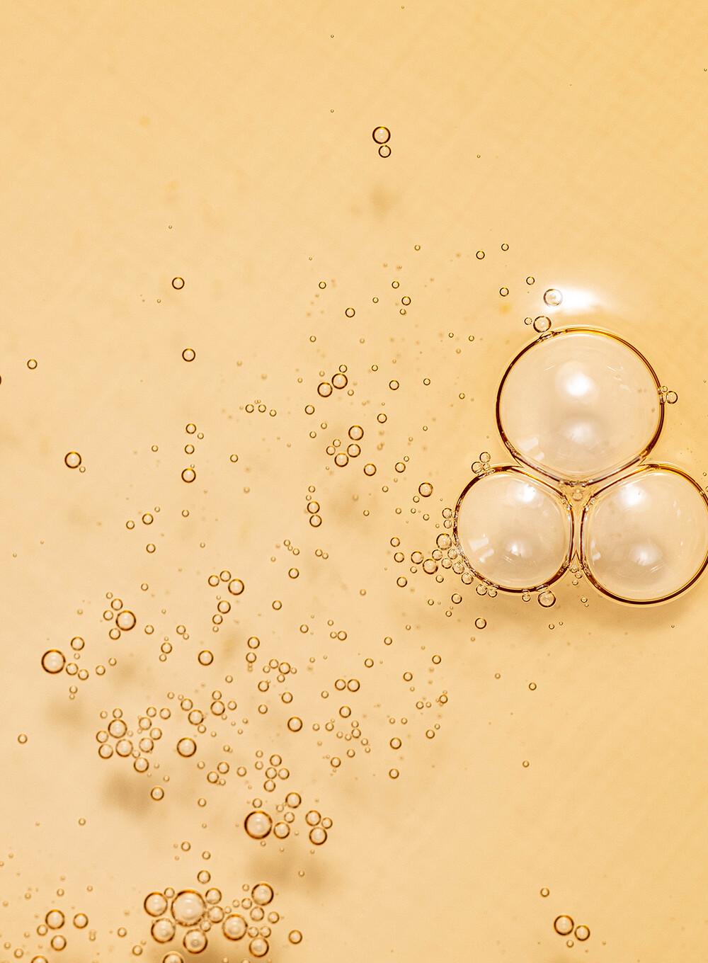 A close-up image of three transparent bubbles clustered together on a light beige background. Numerous smaller bubbles, reminiscent of BEAUTY OF JOSEON - Ginseng Essence Water 150ml by BEAUTY OF JOSEON, are scattered around them, creating a dynamic and airy composition. The scene is minimalistic and has a soft, serene quality.