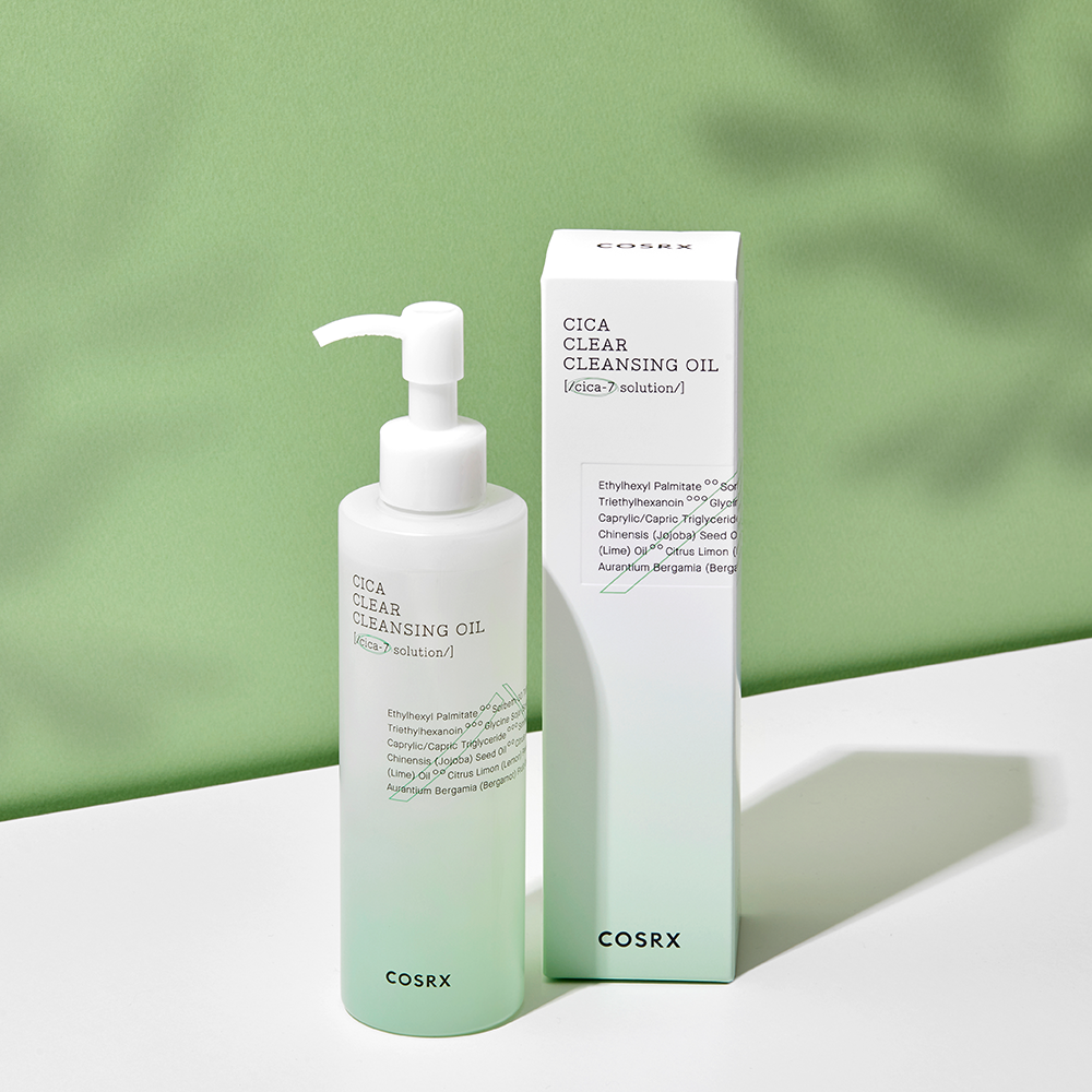 A bottle of COSRX - Pure Fit Cica Clear Cleansing Oil 200ml with a pump dispenser is positioned next to its corresponding packaging box. Both are placed against a green background, casting subtle shadows. Designed for sensitive skin, the product design is minimal with white and green accents.