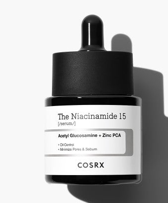 A black dropper bottle of COSRX - The Niacinamide 15 Serum 20ml. The white label lists key ingredients, Acetyl Glucosamine and Zinc PCA, and highlights benefits like oil control, minimizing pores, and acne care. The bottle casts a shadow against a white background.