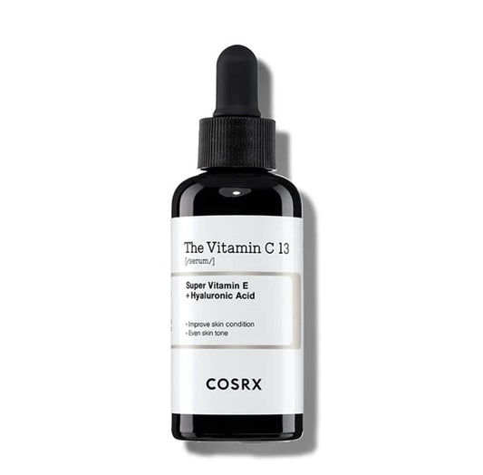 A black dropper bottle with a white label for COSRX - The Vitamin C 13 Serum 20ml, featuring Super Vitamin E and Hyaluronic Acid. The label highlights benefits such as improved skin condition and even skin tone, while also targeting dark spots. The cap is black, and the product name is prominently displayed.