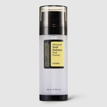 A cylindrical bottle of COSRX - Advanced Snail Radiance Dual Essence 80ml, known for its hydrating and brightening properties, is shown against a plain background. The bottle has a black pump dispenser with a clear cap and a front label displaying the product name. It contains 80 mL (2.70 fl. oz.) of snail essence.