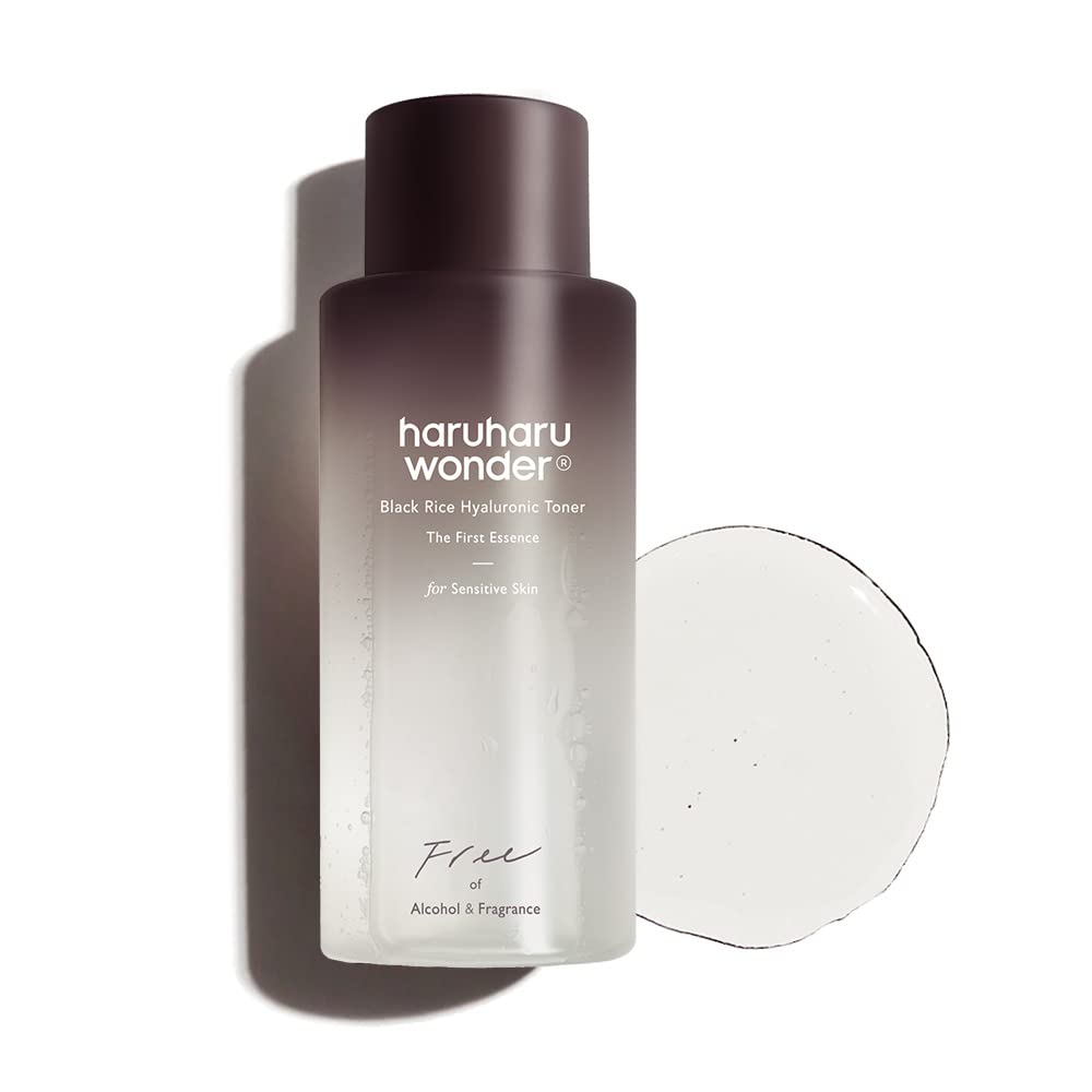 A bottle of HARUHARUWONDER - Black Rice Hyaluronic Toner for Sensitive Skin 150ml from HARUHARU WONDER is displayed next to a clear liquid splash. The hypoallergenic toner fades from dark brown at the top to light gray at the bottom, with text detailing its features and that it provides hydration for sensitive skin and is free of alcohol and fragrance.