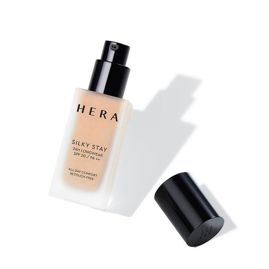 Image of a HERA Silky Stay Foundation 24h Longwear PA++ 30g bottle. The lightweight formula foundation bottle is white with black lettering and a black pump dispenser. The black cap is removed and placed next to the bottle on a white surface, casting a shadow.