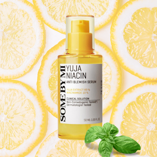 A yellow bottle of SOME BY MI - Yuja Niacin Anti Blemish Care Serum 50ml is placed in the center, surrounded by slices of yuja fruit. There is also a small basil plant at the bottom right. The bottle's label highlights the presence of Yuja extract and Niacinamide for enhanced brightening effects.