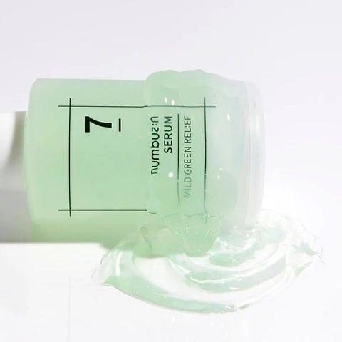 A light green bottle of Numbuzin NUMBUZIN - No. 7 Mild Green Soothing Serum 50ml is lying on its side, with the cap off, and its contents spilling out onto a white surface. The gel-like serum, enriched with Centella Asiatica Extract, deeply hydrates and soothes sensitive skin. The label reads "No. 7 Mild Green Relief Serum.