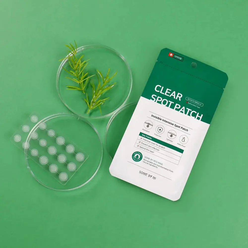 A green flat lay image displays a packet of "SOME BY MI - Clear Spot Patch" alongside a petri dish with small hydrocolloid fabric patches. Another petri dish holds some small green plants. The background is entirely green, complementing the blemish healing product and plants.