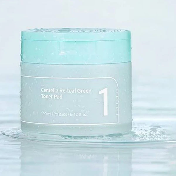 A light blue-lidded container of NUMBUZIN - No.1 Centella Re-Leaf Green Toner Pad 70Pads 190ml with "1" prominent on the front. The jar, perfect for sensitive skin, holds 190 ml or 70 vegan pads (6.4 fl oz) infused with cica extract and is photographed with water droplets and a watery background.
