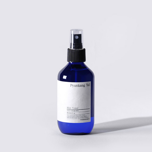 A blue spray bottle labeled "PYUNKANGYUL - Mist Toner 100ml" stands upright against a light gray background. The bottle features a black spray cap and a minimalist white label with black text, emphasizing its role as a hydrating toner in cruelty-free skincare.