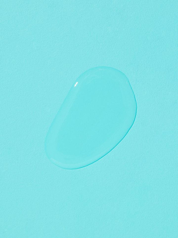 A clear droplet of COSRX - Two in One Poreless Power Liquid 100ml, reminiscent of an essence-toner, sits on a bright turquoise surface. The oval-shaped droplet is smooth with light reflecting off its surface, creating a glossy appearance. The solid, uniform background enhances the droplet's visibility and suggests smooth skin texture and tightened pores.