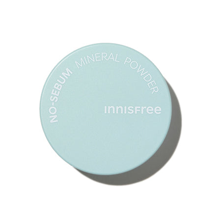 A round, light blue container with the words "INNISFREE - No-Sebum Mineral Powder 5g" and "INNISFREE" printed in white. The sebum-control powder boasts a 10-free clean formula, promising a refined clear look. The container appears plain with a shadow cast on the right side, suggesting it is under a direct light source.